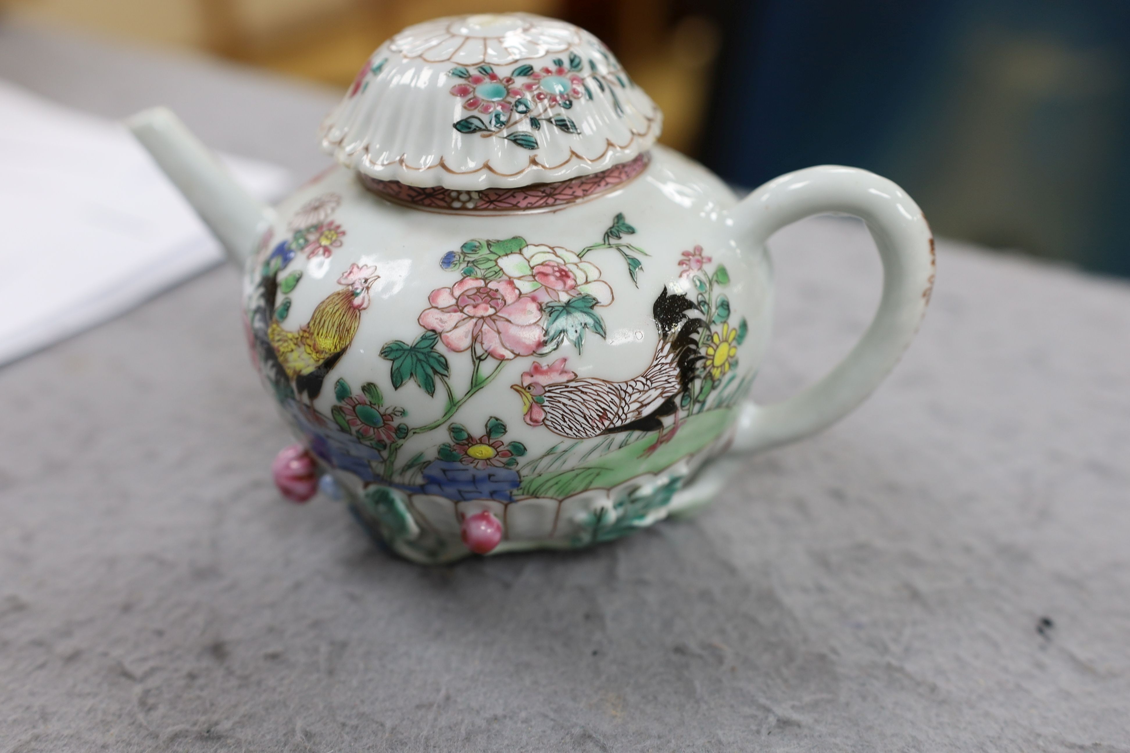 A Chinese famille rose chrysanthemum moulded teapot, early Qianlong period, painted with a cockerel amongst flowers, on a cage work base, 10 cms high